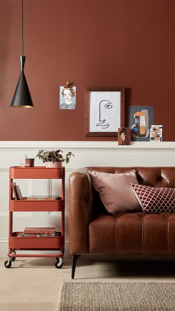 half bold terracotta half white walls natural brown leather sofa movable cart for books gray area rug accent black pendant